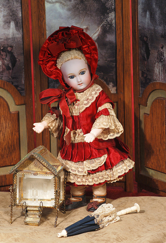 Size 1 Jumeau Bebe with cartouche incised mark in a red silk couturier costume and signed shoes stands aside a fine French glass dollhouse and ivory-handled parasol. Image courtesy Frasher's Doll Auctions.
